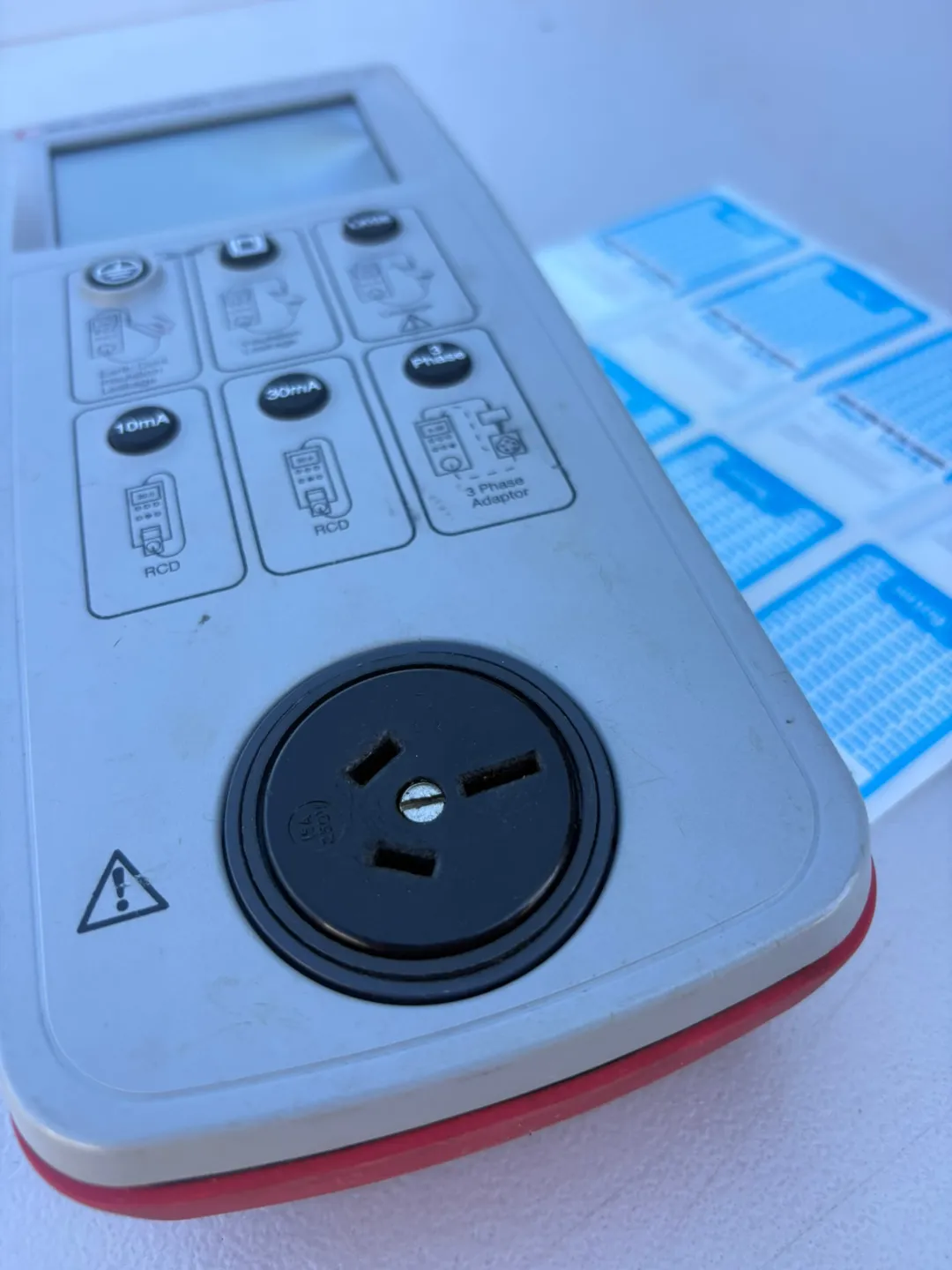 Portable appliance tester with an Australian test socket beside a sheet of blue test and tag labels